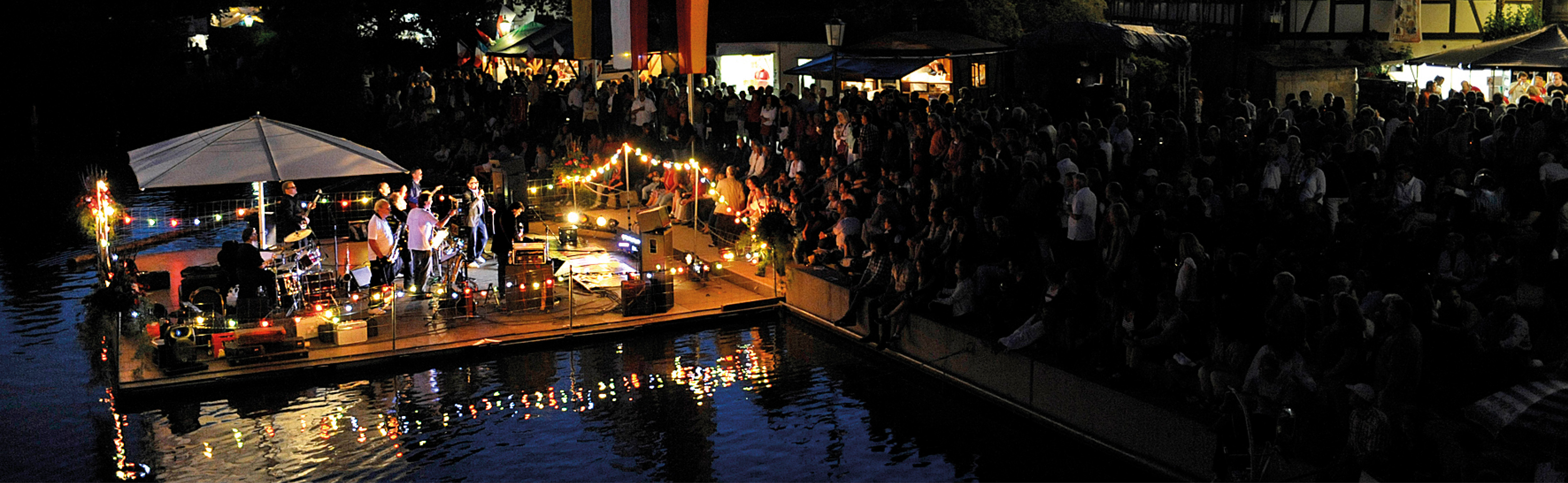 Beleuchtete Bühne mit Band auf dem Neckar und Publikum am Ufer