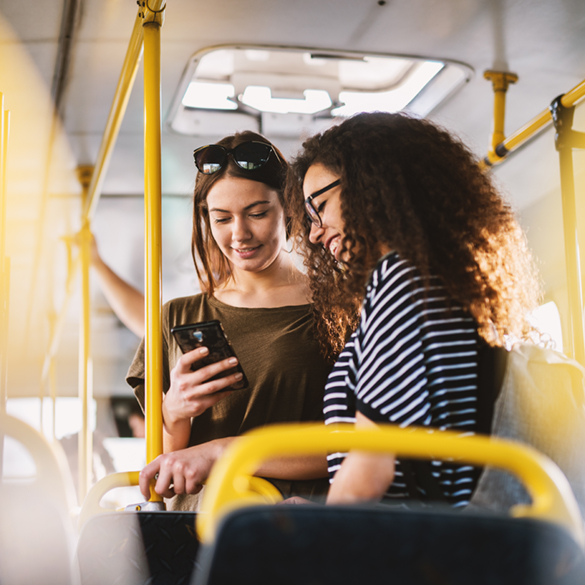 Zwei Frauen stehen im Bus und schauen auf ein Smartphone